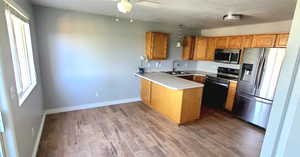 Kitchen with stainless steel appliances, a peninsula, light countertops, brown cabinets, and light wood-type flooring