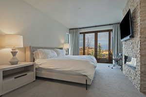 Carpeted bedroom with access to outside, multiple windows, a stone fireplace, and french doors