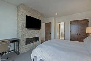 Carpeted bedroom with a stone fireplace, recessed lighting, ensuite bath, and a closet