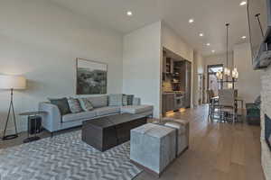 Living room with wood-type flooring, recessed lighting, a stone fireplace, and a chandelier