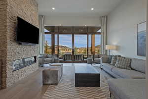 Living room featuring hardwood / wood-style flooring, a wall of windows, recessed lighting, and a stone fireplace