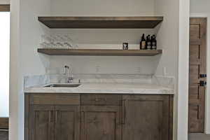Indoor wet bar with open shelves, dark brown cabinetry, and light stone counters