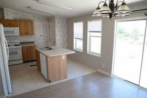 Kitchen with light countertops, white appliances, wallpapered walls, a center island with sink, and decorative light fixtures