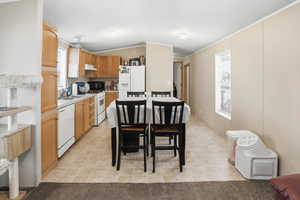 Kitchen featuring light countertops, white appliances, vaulted ceiling, under cabinet range hood, and light brown cabinets