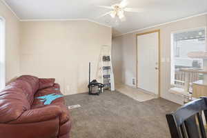 Living room featuring ornamental molding, carpet flooring, a ceiling fan, and vaulted ceiling