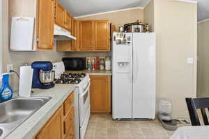 Kitchen with white appliances, light countertops, brown cabinets, under cabinet range hood, and a textured ceiling