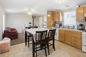 Kitchen with light countertops, white appliances, crown molding, light flooring, and ceiling fan