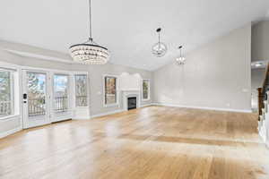 Unfurnished living room with a glass covered fireplace, light wood-type flooring, a chandelier, and high vaulted ceiling