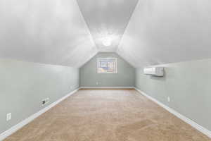 Bonus room featuring vaulted ceiling, light colored carpet, a textured ceiling, and a wall mounted AC