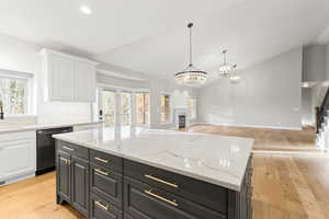Kitchen with dark cabinets, light wood finished floors, a fireplace, decorative light fixtures, and high vaulted ceiling