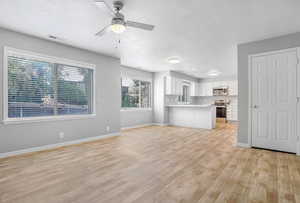 Unfurnished living room with light wood-type flooring, a textured ceiling, and a ceiling fan