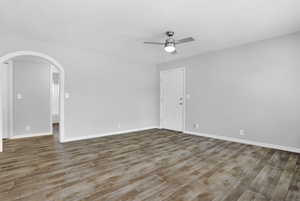 Empty room with arched walkways, wood finished floors, and ceiling fan
