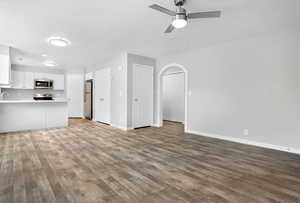 Unfurnished living room with dark wood-type flooring, arched walkways, and a ceiling fan