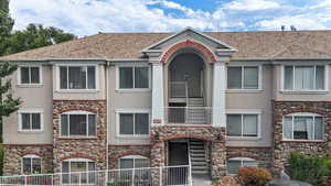 View of front of property featuring stone siding, stucco siding, and a balcony