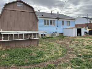 Back of house with a storage shed, roof with shingles, and board and batten aluminum siding.