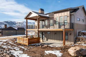 Snow covered property featuring board and batten siding, a patio, a deck with mountain view, and a chimney