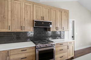 Kitchen featuring gas stove, light brown cabinets, decorative backsplash, dark wood-style flooring, and vaulted ceiling