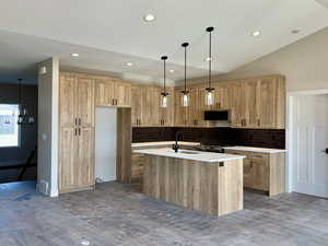 Kitchen featuring backsplash, hanging light fixtures, a kitchen island with sink, recessed lighting, and vaulted ceiling
