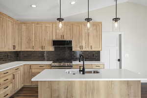 Kitchen featuring light brown cabinets, high end stainless steel range, pendant lighting, dark wood-style flooring, and a kitchen island with sink