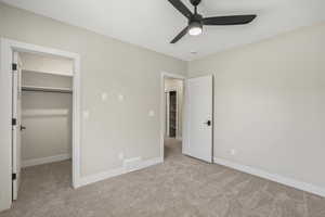Unfurnished bedroom with a walk in closet, carpet floors, and a ceiling fan