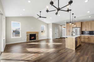 Kitchen with open floor plan, a center island with sink, a stone fireplace, dark wood finished floors, and lofted ceiling