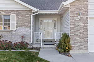 Property entrance featuring brick siding, a shingled roof, and a garage