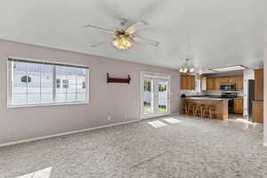 Kitchen featuring brown cabinets, open floor plan, a kitchen bar, light carpet, and black / electric stove