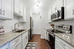 Kitchen with appliances with stainless steel finishes, light stone counters, white cabinetry, and dark wood-style flooring