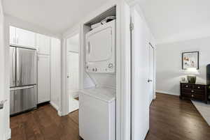 Washroom with dark wood-style floors and stacked washer / dryer