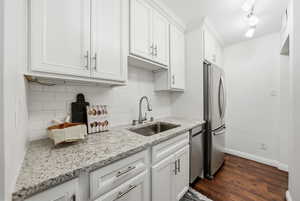 Kitchen with white cabinetry, decorative backsplash, light stone counters, dark wood-style floors, and stainless steel appliances