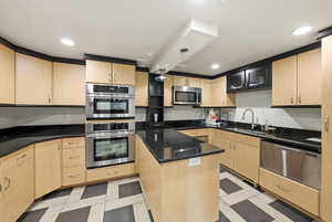 Kitchen featuring light brown cabinets, stainless steel appliances, dark stone countertops, light floors, and recessed lighting