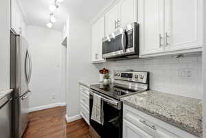 Kitchen featuring appliances with stainless steel finishes, white cabinetry, light stone counters, and dark wood finished floors