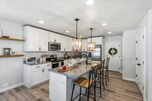 Kitchen featuring a breakfast bar area, white cabinetry, stainless steel appliances, dark stone countertops, and a kitchen island with sink