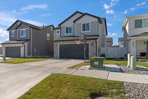 View of front facade with board and batten siding, stone siding, an attached garage, driveway, and a front lawn