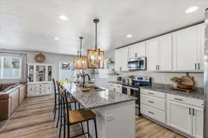 Kitchen with a kitchen bar, stainless steel appliances, light stone countertops, white cabinets, and a center island with sink