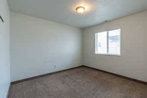 Carpeted empty room with a textured ceiling and baseboards