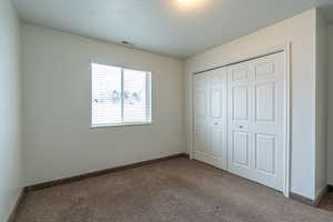 Unfurnished bedroom featuring a textured ceiling, carpet floors, and a closet