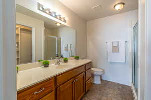 Full bath featuring vanity, a shower stall, stone finish flooring, a textured ceiling, and a walk in closet