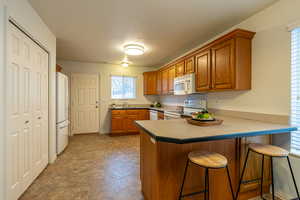 Kitchen with a breakfast bar, brown cabinetry, a peninsula, white appliances, and a textured ceiling
