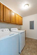 Laundry area featuring stone finish flooring, cabinet space, a textured ceiling, washer and clothes dryer, and electric panel