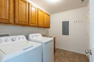Laundry area featuring stone finish flooring, electric panel, cabinet space, independent washer and dryer, and a textured ceiling
