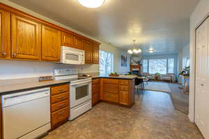 Kitchen with a peninsula, white appliances, brown cabinetry, dark countertops, and pendant lighting