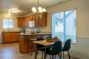 Kitchen featuring brown cabinets, decorative light fixtures, a textured ceiling, white appliances, and a peninsula