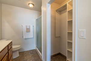 Full bath featuring a shower stall, a textured ceiling, stone finish flooring, a spacious closet, and vanity