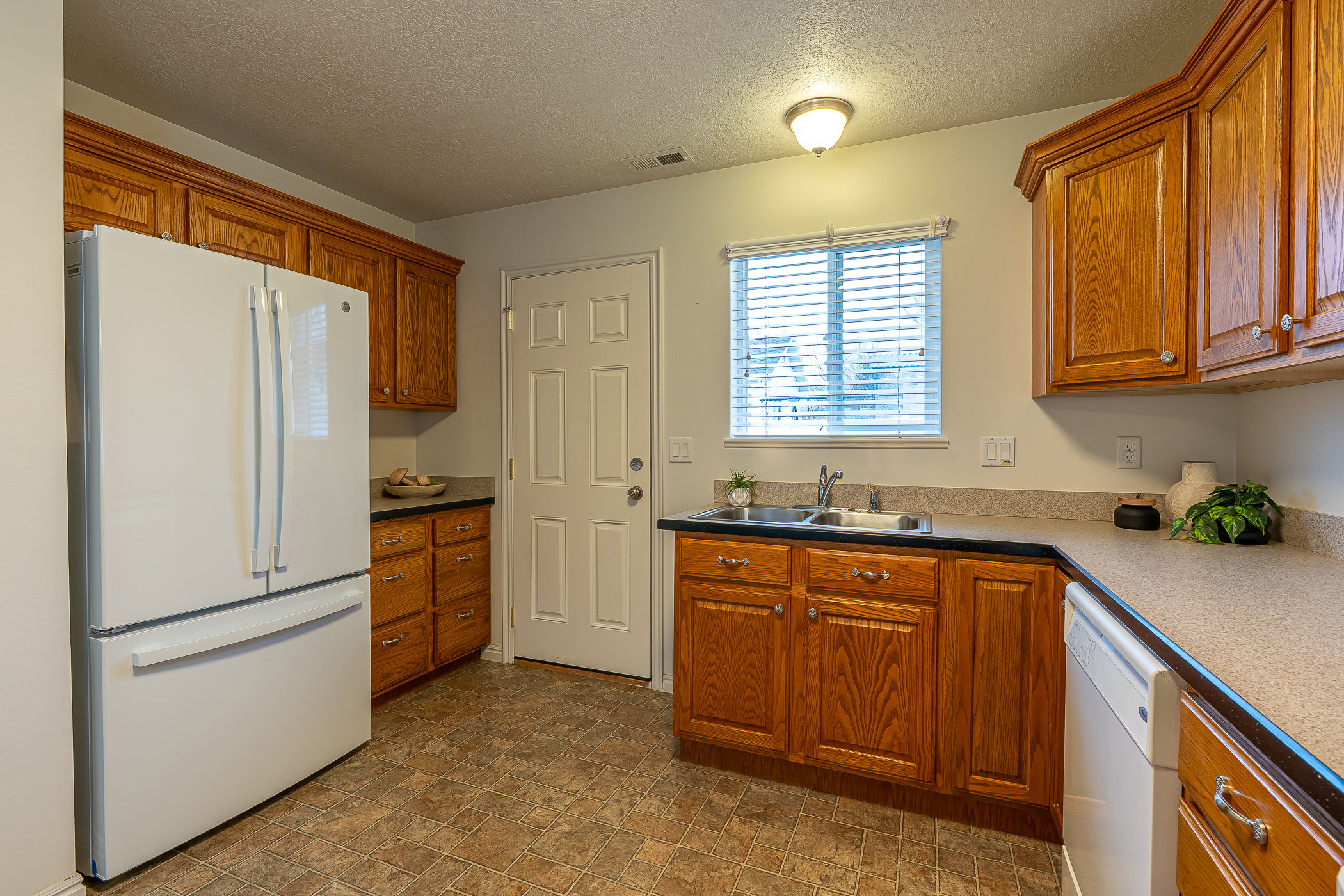 Kitchen featuring white appliances, a textured ceiling, brown cabinetry, and stone finish flooring
