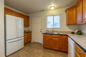 Kitchen featuring white appliances, a textured ceiling, brown cabinetry, and stone finish flooring
