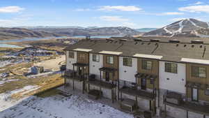 Snow covered house featuring a mountain view, a patio area, and a shingled roof