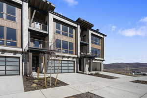 View of front of property with stone siding, driveway, a balcony, a mountain view, and an attached garage