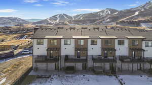 Snow covered house with a mountain view, roof with shingles, and a patio area