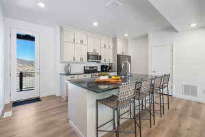 Kitchen with an island with sink, a breakfast bar area, light wood-style flooring, stainless steel appliances, and recessed lighting